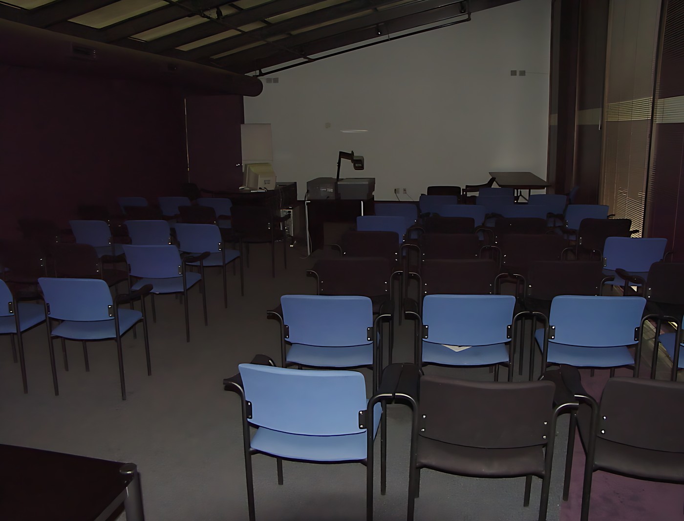 Empty auditorium with rows of blue chairs facing a projector screen