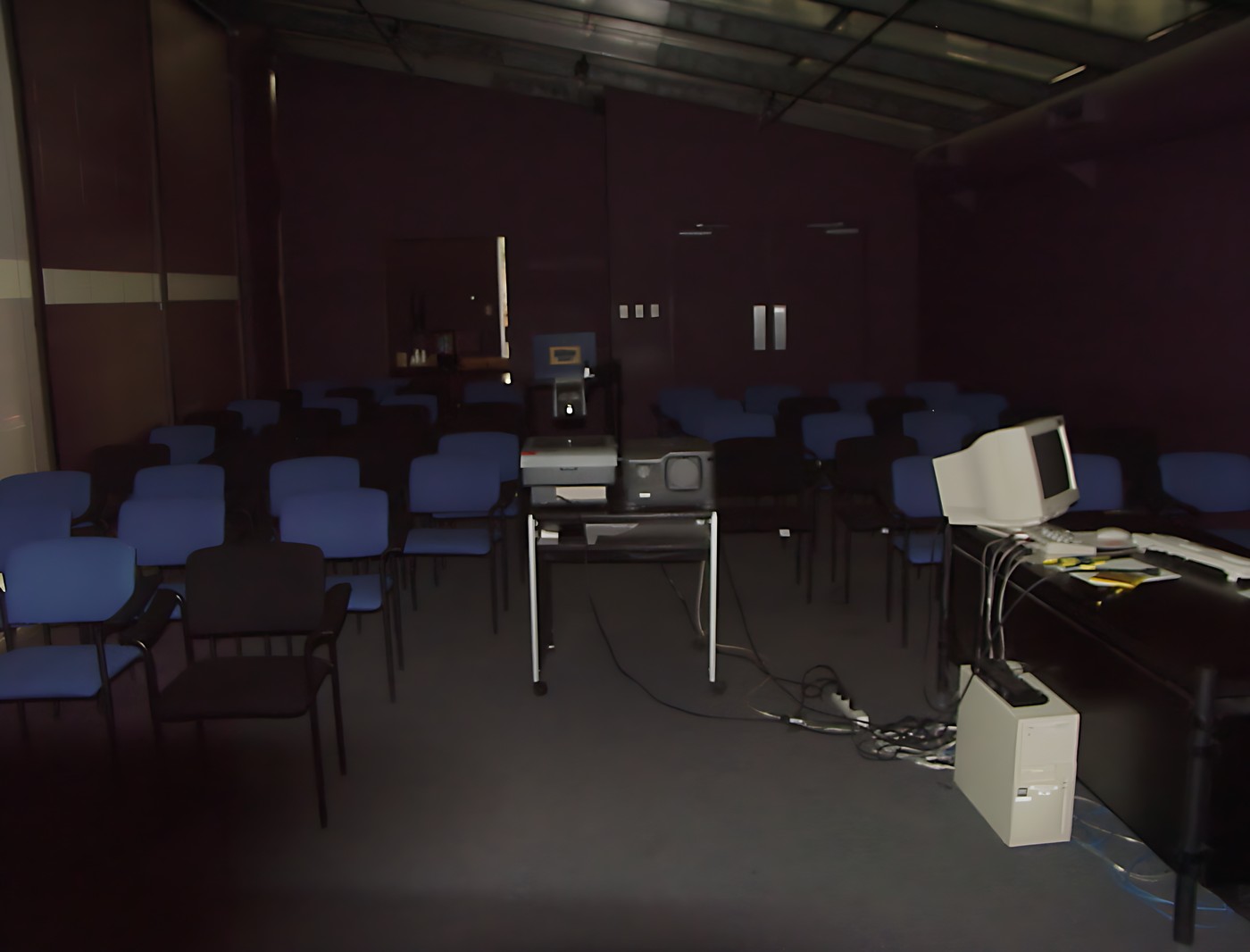 Empty lecture hall with rows of blue chairs facing the front of the room